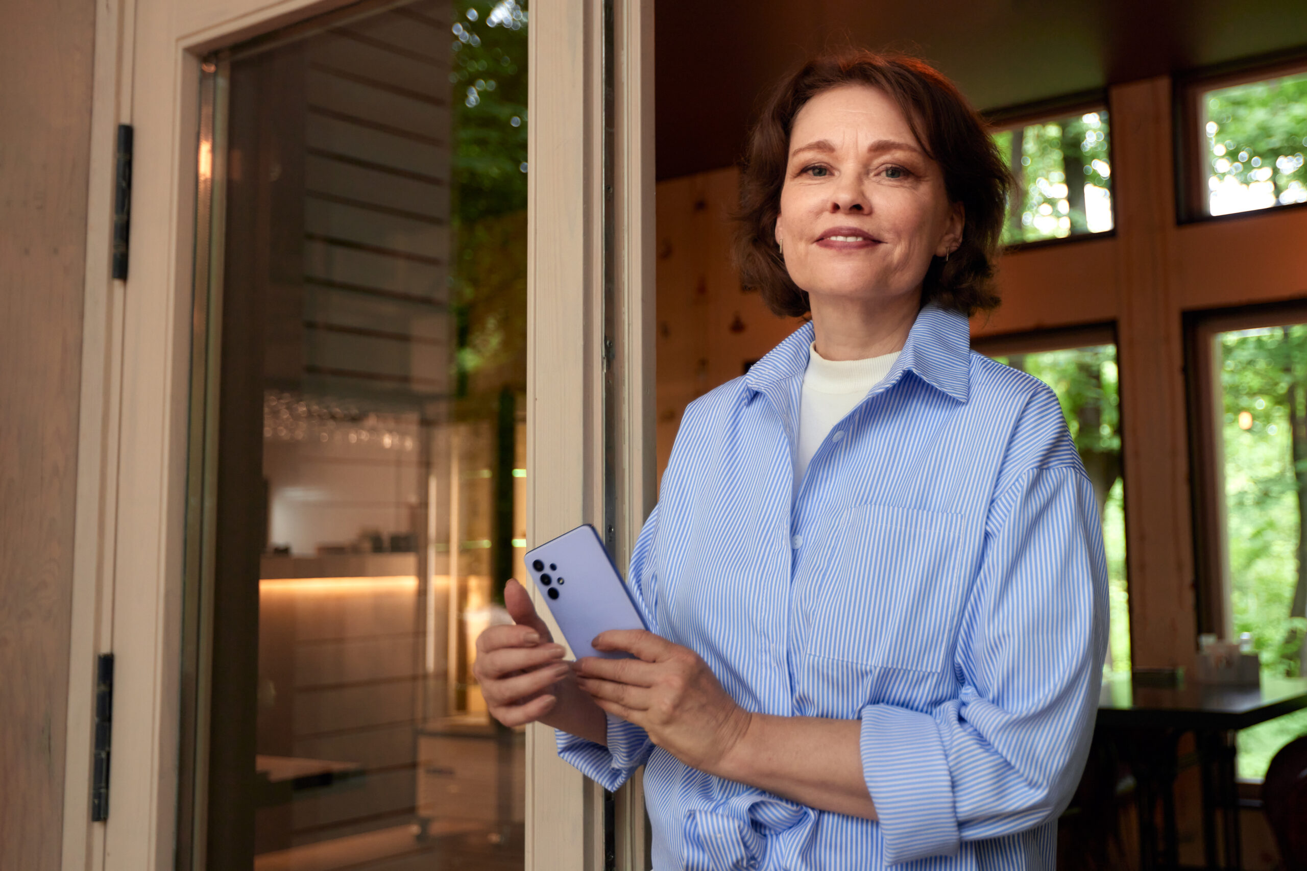 Portrait of an attractive smiling elderly woman. Mature caucasian woman with smartphone. Middle-aged brunette in casual clothes on the porch of a country cottage. Active lifestyle for the elderly.