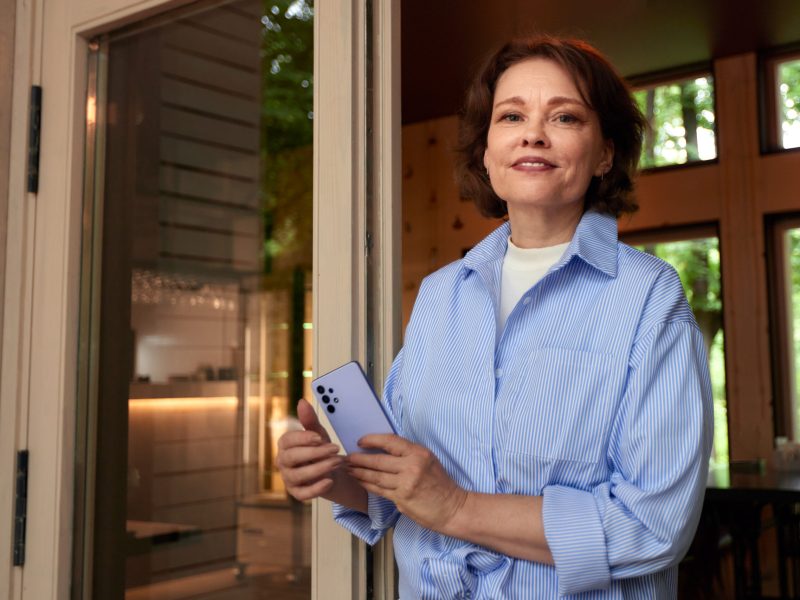 Portrait of an attractive smiling elderly woman. Mature caucasian woman with smartphone. Middle-aged brunette in casual clothes on the porch of a country cottage. Active lifestyle for the elderly.